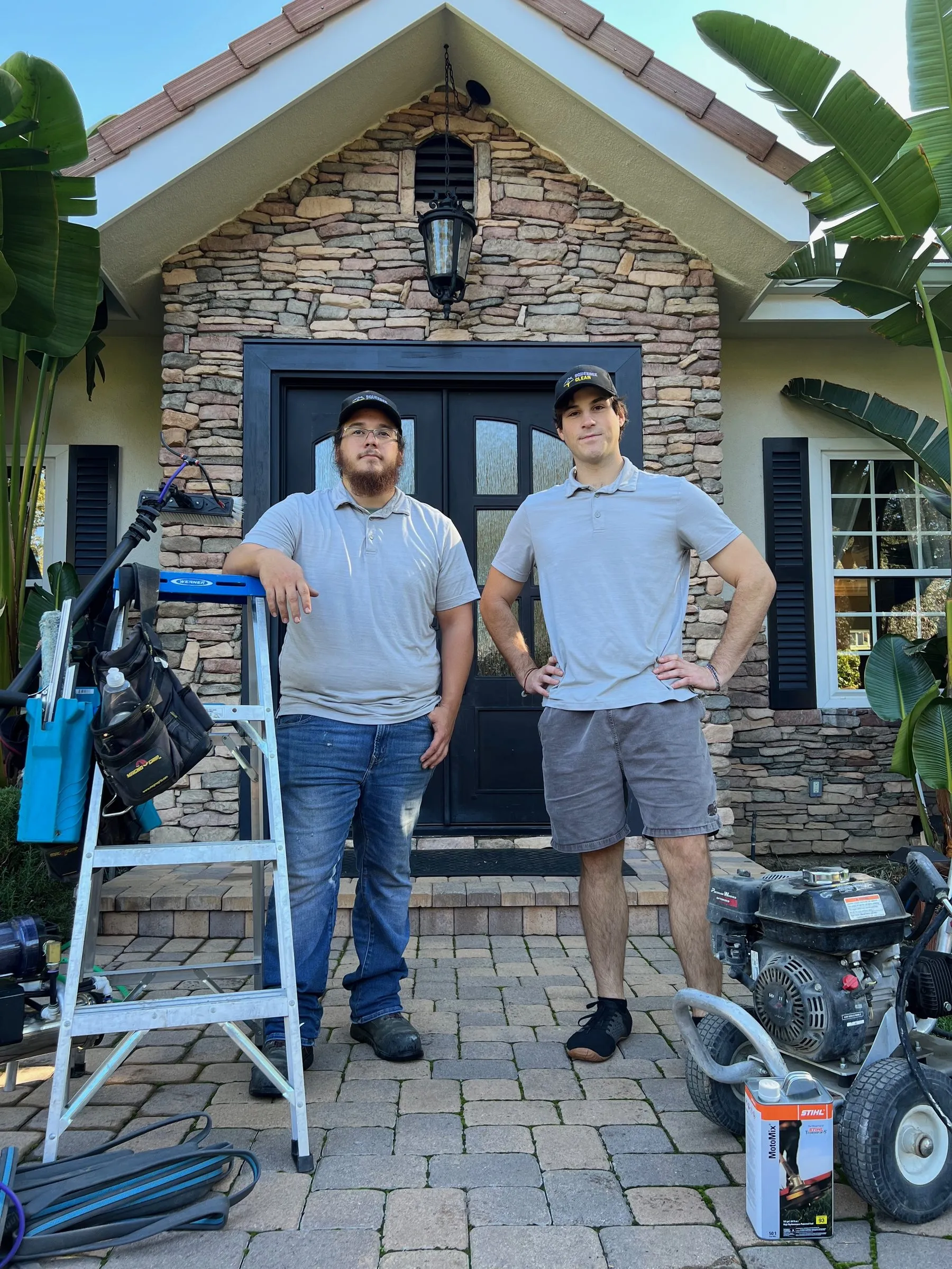 Two crew members in uniform at a customer's front door with a ladder and pressure washer