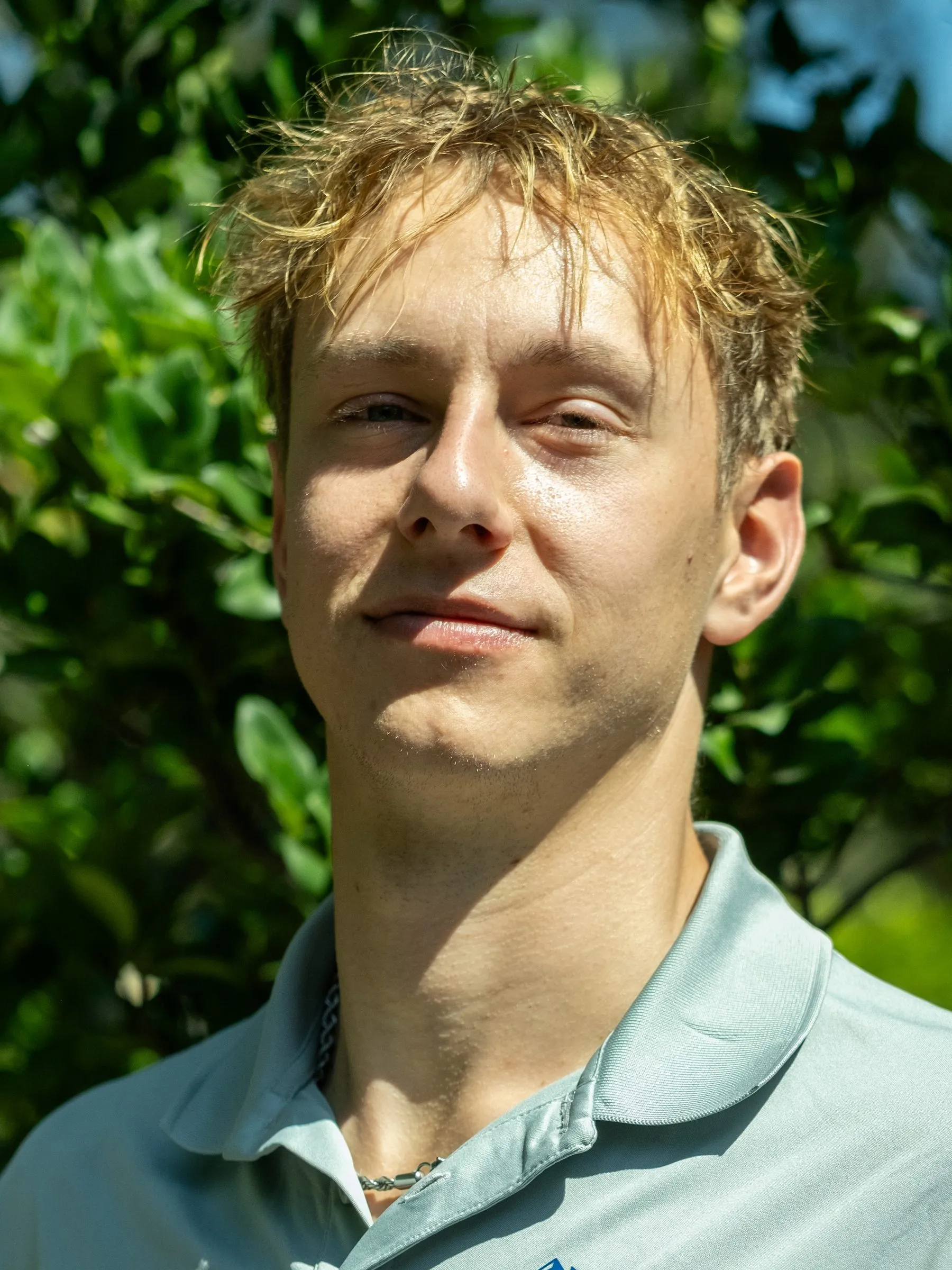 Jordan, founder of Squeegee Clean Windows, in a logo polo in front of greenery