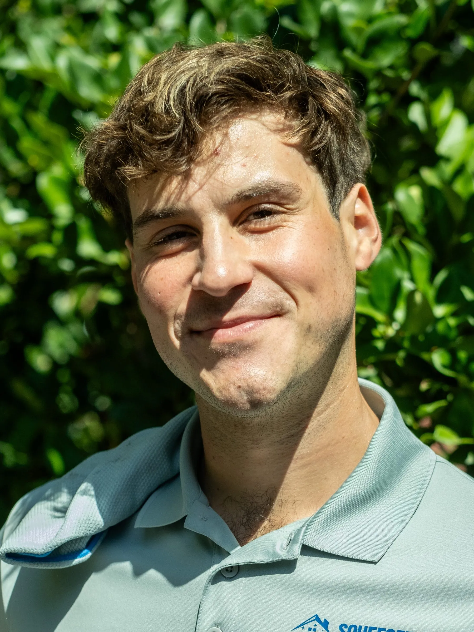 Elliott Kenny, owner of Squeegee Clean Windows, in a logo polo in front of greenery