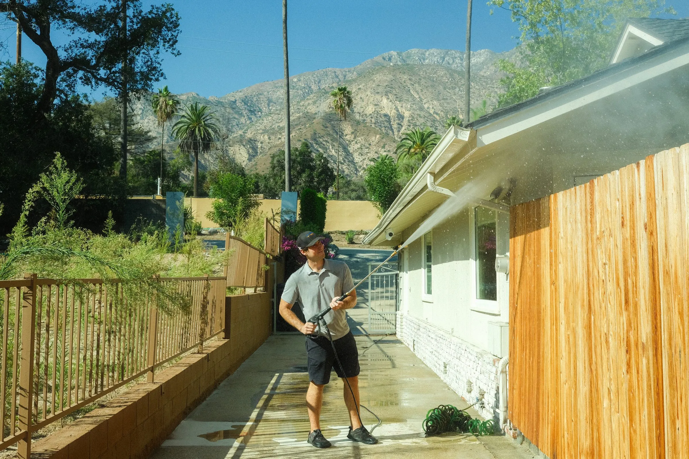 Elliot washing the eaves of a white ranch house, mountains behind