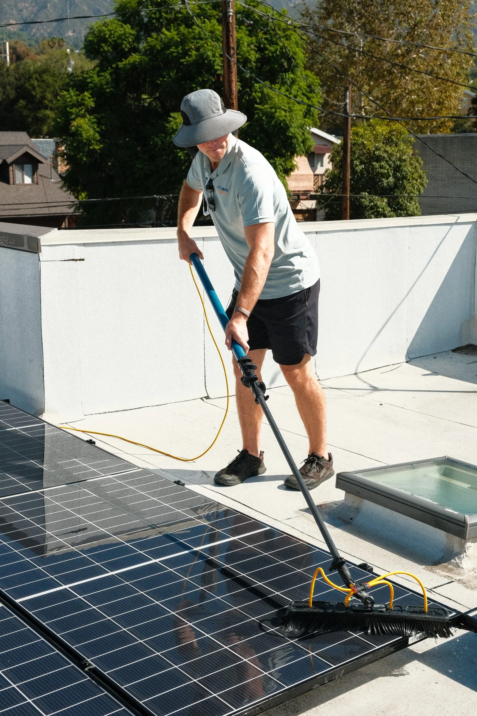 Elliot brushing rooftop solar panels with a water-fed pole