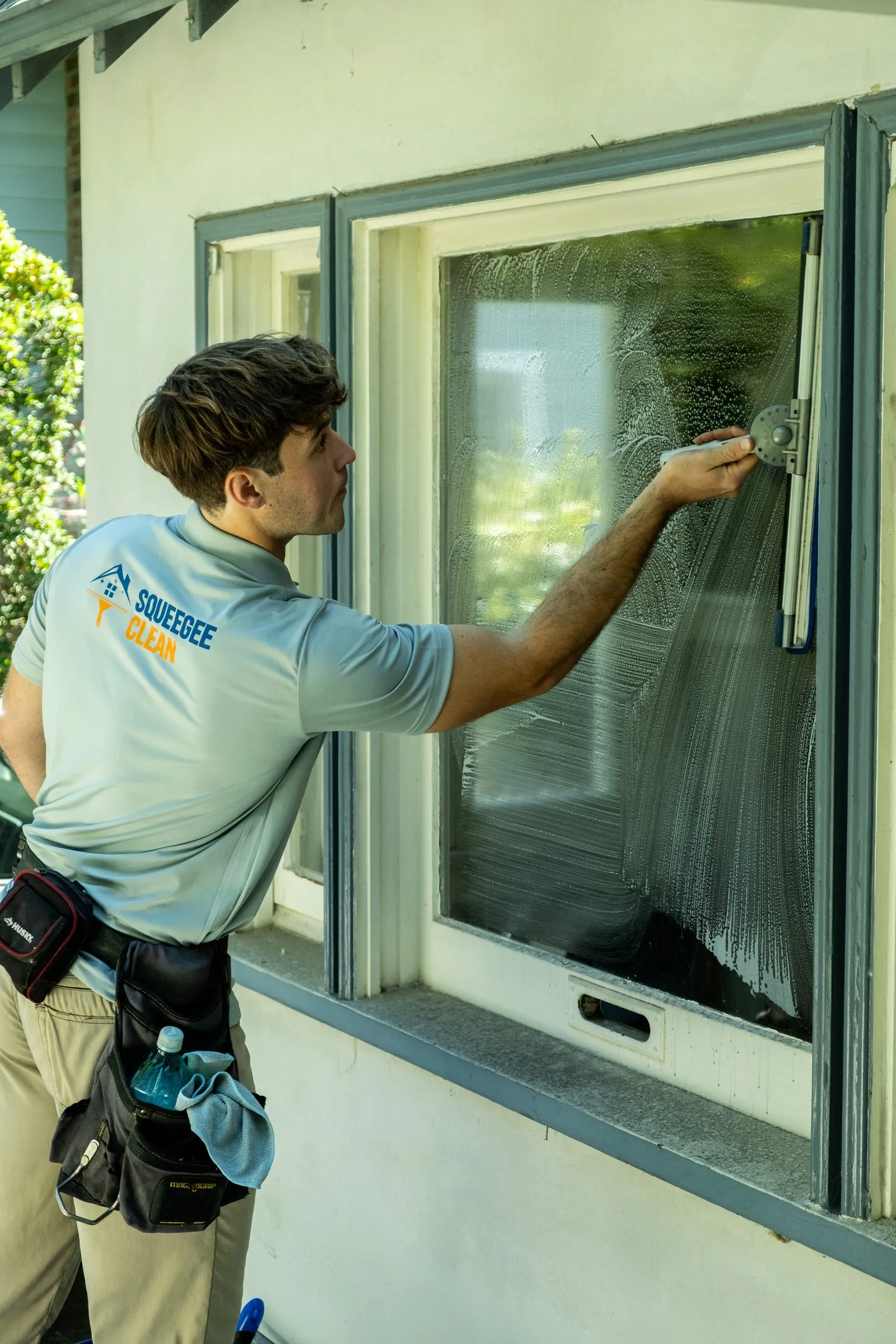 Elliott wiping down a window frame by hand, tool belt on