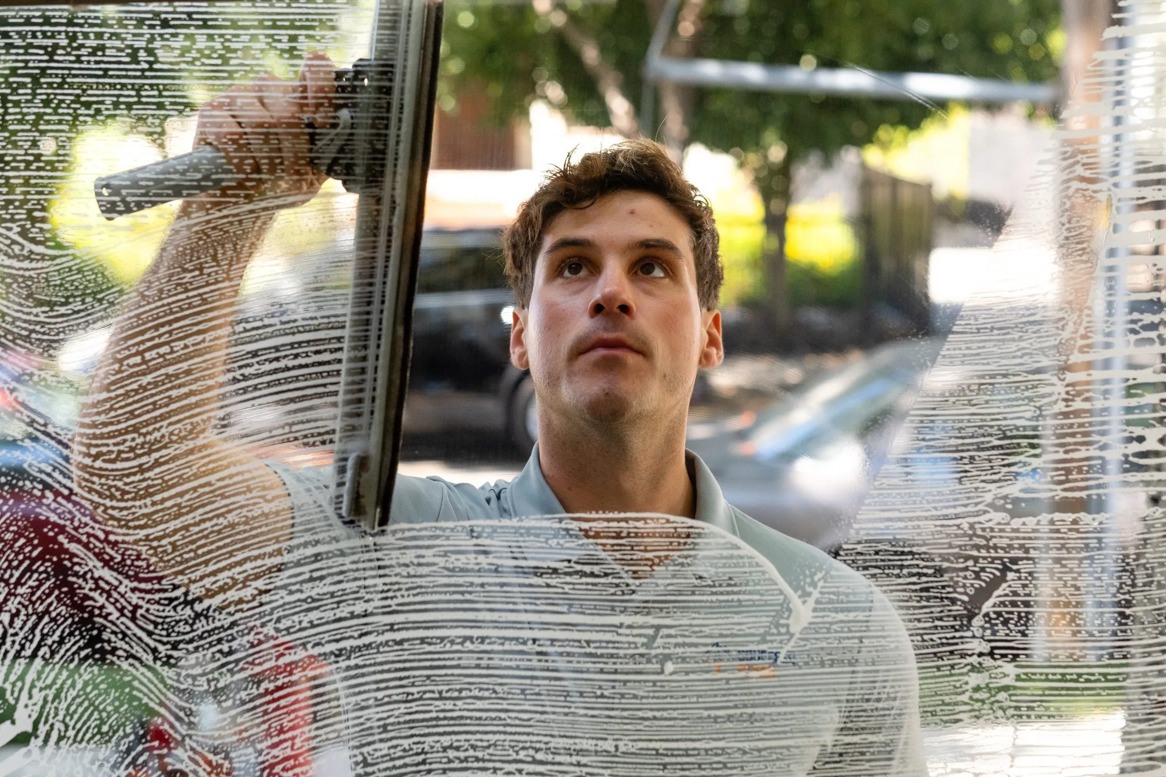 Elliott seen through a soapy window, squeegee in hand, looking up at the top of the pane